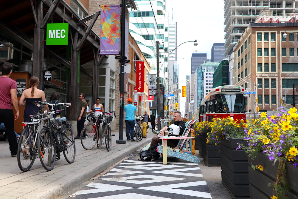 People sitting and walking along King St, with streetcar in background and flowers in foreground.