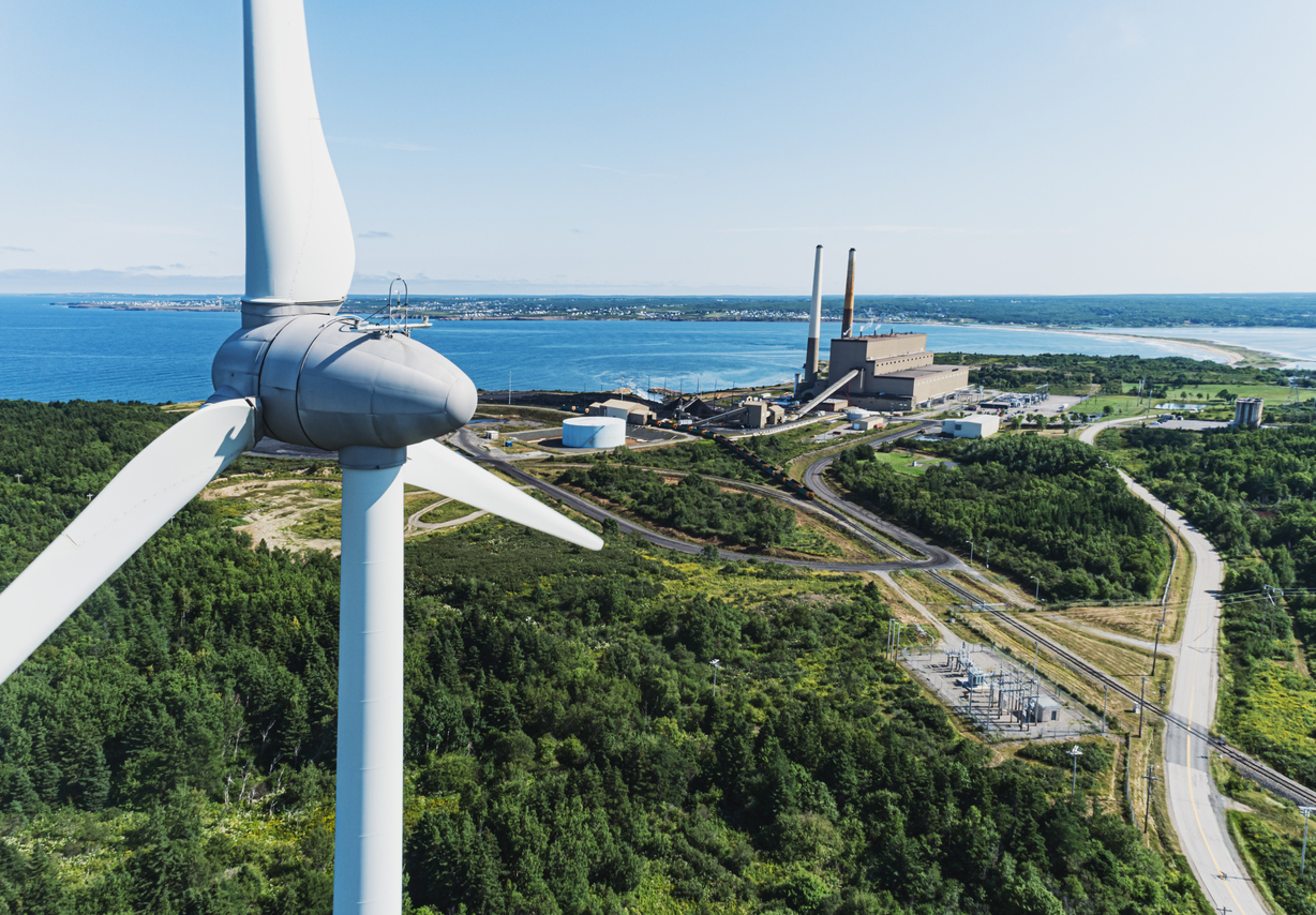 Aerial drone view of a wind turbine in the foreground of a coal fired power generating station.