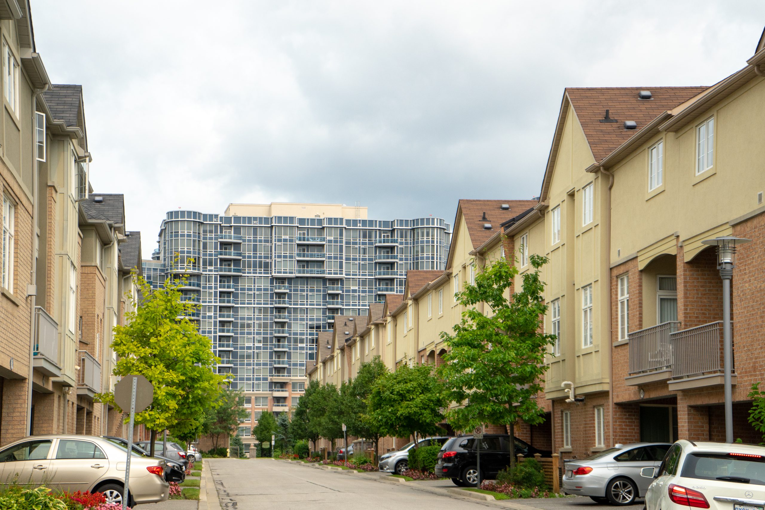 A row of beige townhouses on either side of a street, with a taller condo building in the background